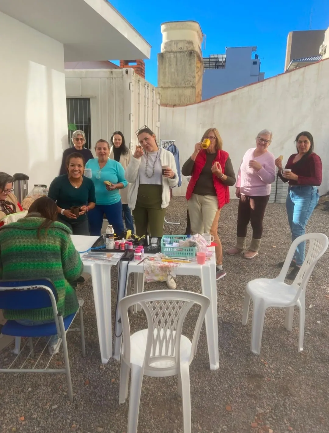 Voluntárias do Bazar Mãos Criativas no pátio da casa, em volta de mesas brancas com peças de artesanato.